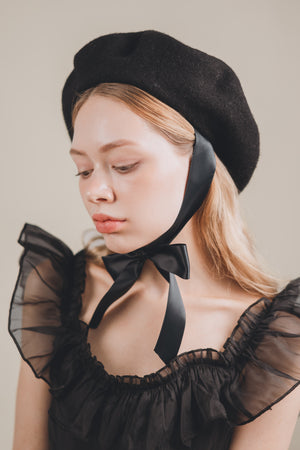 Woman wearing a black beret and black lace garment against a neutral background