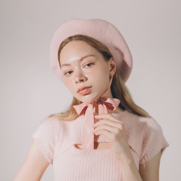 

Woman wearing a pink knit top and beret with a bow tie against a plain background
